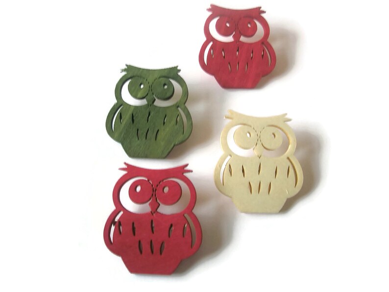 May include: Four wooden owl ornaments in different colors: red, green, cream, and brown. The owls have large eyes and a simple design.
