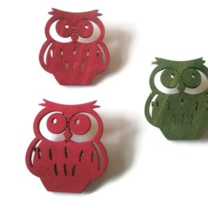 May include: Three wooden owl ornaments, one red, one green, and one red. The owls are cut out and have a simple design.
