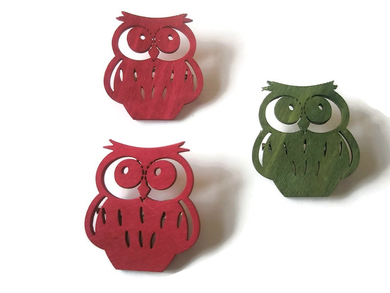 May include: Three wooden owl ornaments, one red, one green, and one red. The owls are cut out and have a simple design.