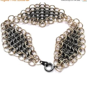 Könnte beinhalten: Ein schwarzes und goldenes Kettenhemdarmband mit einem Verschluss. Das Armband besteht aus kleinen Metallringen, die miteinander verbunden sind.