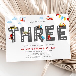 Puede incluir: Una invitación de cumpleaños blanca con un diseño de carretera gris y negro que forma la palabra "TRES". La invitación presenta vehículos de dibujos animados coloridos y el texto "What fun to be" en la parte superior. El texto "Hit the road and join us to celebrate Oliver's Third Birthday" está en rojo. La invitación incluye la fecha, la hora, la ubicación y la información de RSVP.