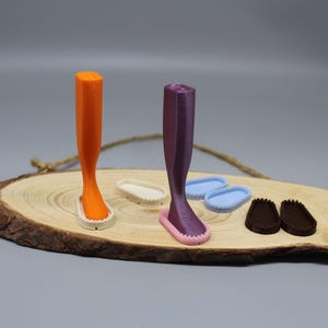 Puede incluir: Cuatro pares de zapatos en miniatura impresos en 3D sobre una superficie de madera. Los zapatos son de color naranja, morado, blanco y azul.