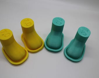 May include: Four boot-shaped molds arranged in a row, consisting of two yellow molds and two teal molds. Each mold features a flat top surface with the number 7.0 embossed into the material. The molds have a smooth, matte finish and a distinct raised rim around the base, designed for crafting or casting purposes.