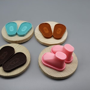 May include: Four sets of miniature shoes on wooden bases. The shoes are in four different colours: brown, blue, pink, and orange. Each set has two shoes with the letters "FR" on the bottom.
