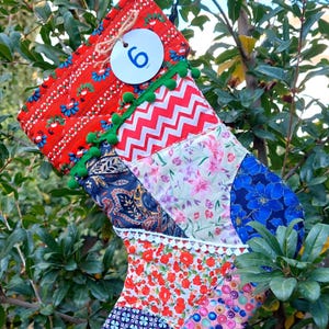 May include: A patchwork Christmas stocking with a red, white, blue, and green color scheme. The stocking has a white tag with the number "6" on it.