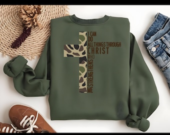 May include: A green sweatshirt with a camouflage cross design. The cross has the words "I can do all things through Christ who strengthens me" written on it.