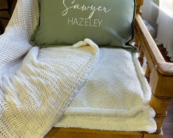 May include: A green pillow with white text that reads "Sawyer HAZELELY" on a wooden chair with a white blanket.