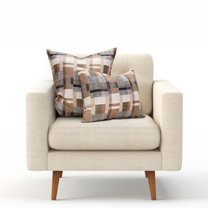 May include: A beige armchair with two patterned throw pillows. The pillows have a brown, black, and pink plaid design.