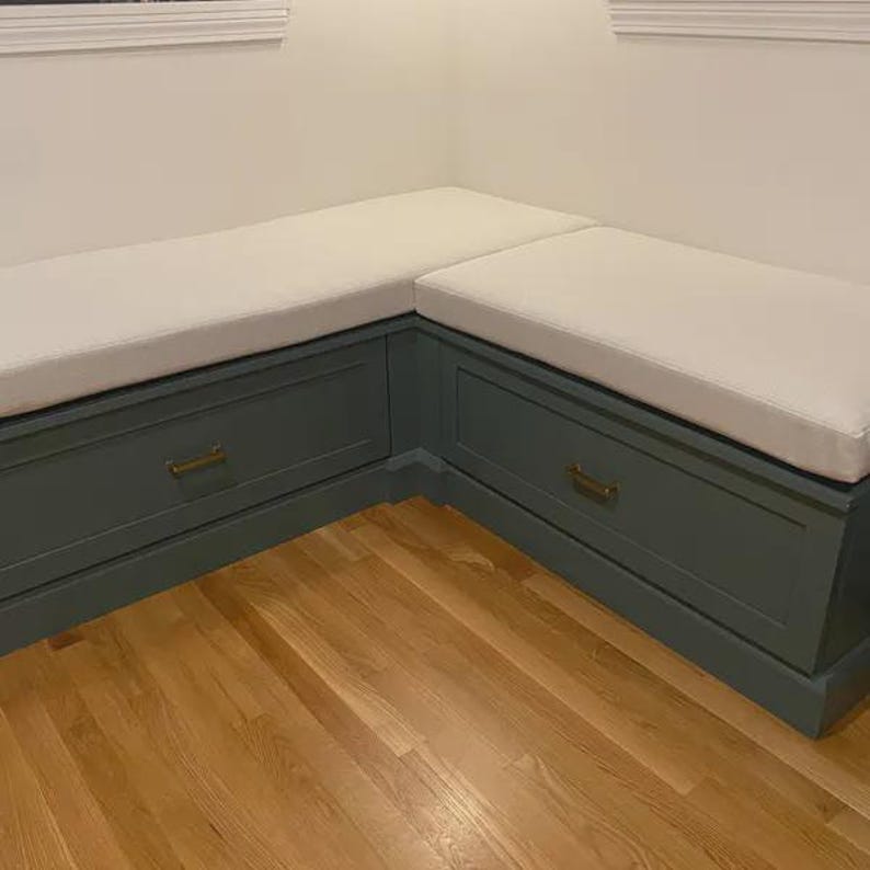 Custom corner bench cushions in light neutral fabric on blue built-in window seating with brass drawer pulls. Perfect for dining nook or mudroom seating, handcrafted by The Hearth & Home Store.