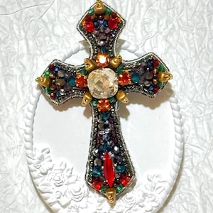 May include: A colourful jeweled cross pendant with a large clear crystal in the centre. The cross is decorated with red, orange, yellow, green, blue, and purple rhinestones.