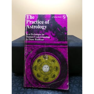 May include: A vintage paperback book titled "The Practice of Astrology" by Dane Rudhyar. The cover is predominantly purple with a circular astrological chart in gold and white. The book is a Pelican Book.