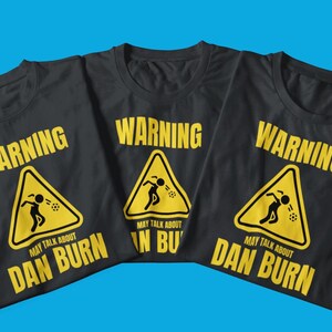 May include: Three black t-shirts with a yellow warning sign graphic. The sign says "Warning May Talk About Dan Burn".