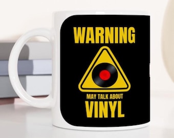 May include: White ceramic mug with a black background and yellow warning sign. The sign has a black vinyl record inside and the text "WARNING MAY TALK ABOUT VINYL".