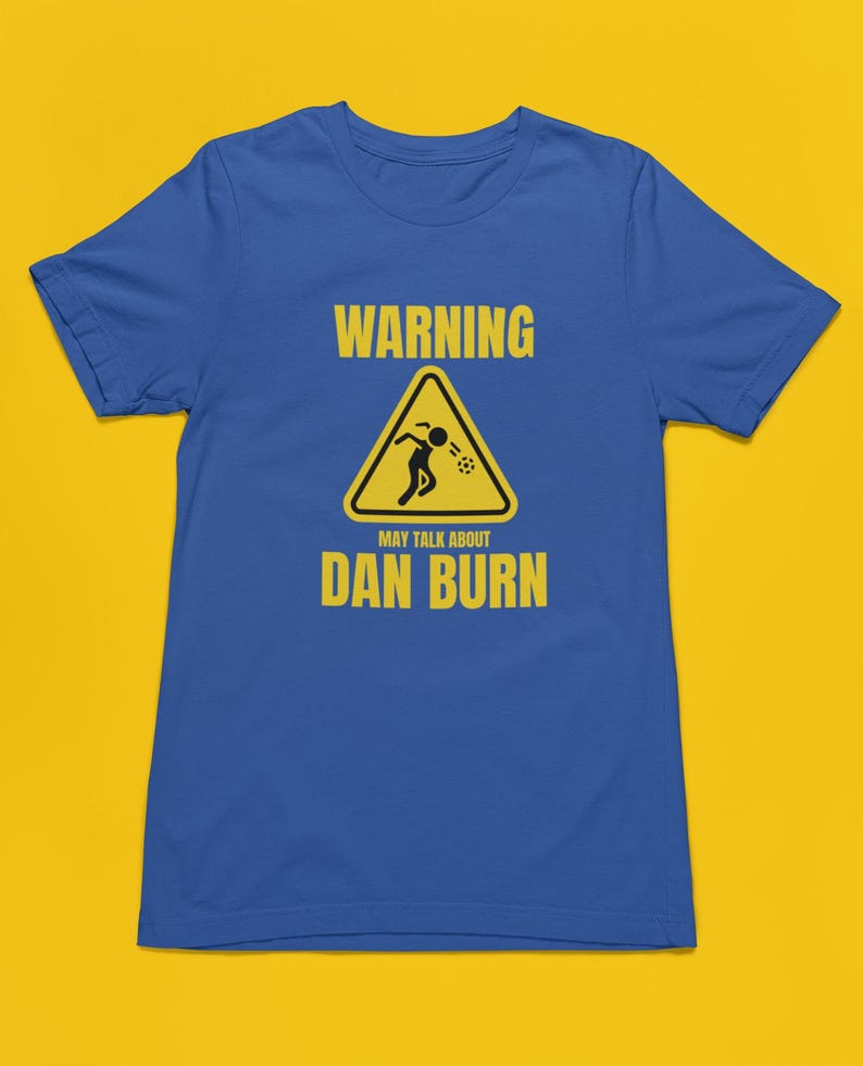May include: A blue t-shirt featuring a yellow warning sign that reads "WARNING MAY TALK ABOUT DAN BURN". The sign depicts a stick figure vomiting.