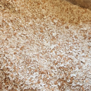 以下が含まれることがあります： 細かく砕かれた卵の殻の山をクローズアップで写した写真。殻は白と茶色の混合で、細かく粉砕されています。