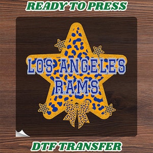 May include: A DTF transfer featuring a large gold glitter star with a blue leopard print pattern. The text LOS ANGELES RAMS is centered in blue block letters. Four smaller stars and a bow with a leopard print design accent the main star.