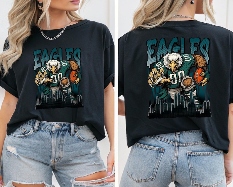 May include: Black t-shirt with a graphic of an eagle in a football uniform holding a football. The word "EAGLES" is above the eagle in teal letters. A cityscape silhouette is at the bottom of the graphic.