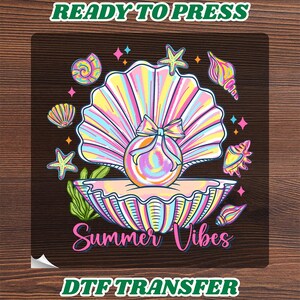May include: A DTF transfer sheet featuring a central iridescent pearl inside an open seashell, surrounded by starfish, various seashells, and green seaweed. The design includes the text READY TO PRESS at the top and Summer Vibes at the bottom.