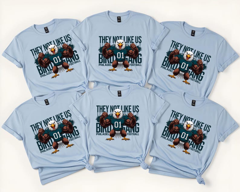 K&ouml;nnte beinhalten: Hellblaue T-Shirts mit einer Grafik eines muskul&ouml;sen Adlers, der ein Football-Trikot tr&auml;gt. Der Text auf den Shirts lautet "THEY NOT LIKE US BIRD GANG PHILADELPHIA FOOTBALL" und "01".