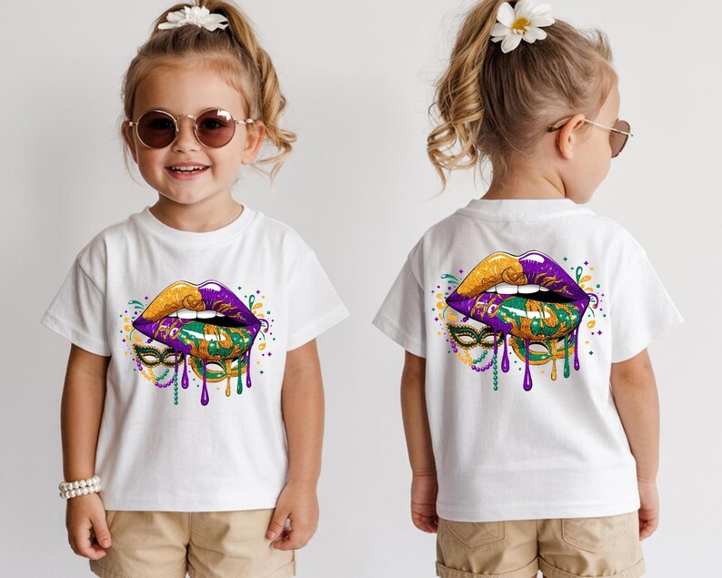 May include: White t-shirt featuring a vibrant graphic of stylized lips in gold, purple, and green, with dripping accents and a mask design. The design is on the front and back of the shirt. The shirt is worn by a child.