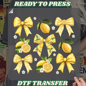 May include: DTF transfer sheet featuring a design of yellow bows, lemons, and white flowers. The bows have polka dot and gingham patterns. The text "READY TO PRESS" and "DTF TRANSFER" are in green.