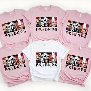 May include: A collection of pink and white t-shirts featuring a graphic design with horror movie characters and the word "FRIENDS" in a stylized font. The shirts are short-sleeved and made of a soft material.
