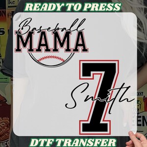 May include: White DTF transfer with the words "Baseball MAMA" in black and red, a baseball graphic, the number 7, and the name "Smith". The text "READY TO PRESS" and "DTF TRANSFER" are also included.