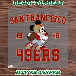 May include: A DTF transfer sheet featuring a graphic of a cartoon mouse wearing a gold and red football helmet and jersey, holding a brown football. The text reads SAN FRANCISCO, 19 46, and 49ERS in red and gold, with READY TO PRESS DTF TRANSFER.