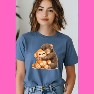 Op de afbeelding: Een blauw t-shirt met een aquarel illustratie van twee knuffelende apen. E&eacute;n aap is bruin, de andere oranje. De apen zitten op een wit oppervlak.