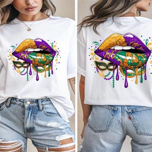 May include: White t-shirt featuring a vibrant graphic of stylized lips in gold and purple, with a green and gold mask design. The design includes dripping purple accents and decorative elements, creating a festive look.