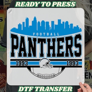 May include: A DTF transfer sheet featuring a blue city skyline silhouette above the word PANTHERS in bold black letters. Below, a football helmet and ball graphic are flanked by the year 1993. The text READY TO PRESS and DTF TRANSFER appears.