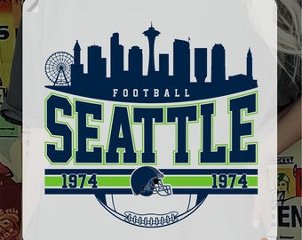 May include: A DTF transfer featuring a Seattle football design. The design includes a navy blue skyline, the word "SEATTLE" in green and navy, and a football helmet. The text "READY TO PRESS" and "DTF TRANSFER" are also present.