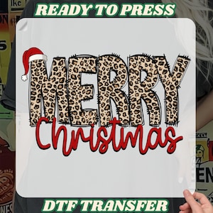 May include: A white DTF transfer featuring the words "MERRY CHRISTMAS" in a leopard print design with a Santa hat on the letter "M". The phrases "READY TO PRESS" and "DTF TRANSFER" are printed above and below the main text.
