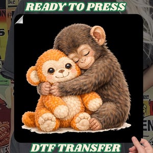 Op de afbeelding: Een DTF-transfer met een bruine aap die een oranje pluche aap omhelst. De bruine aap heeft zijn ogen gesloten en de oranje aap heeft grote, vriendelijke ogen. De woorden "READY TO PRESS" en "DTF TRANSFER" staan op de afbeelding.