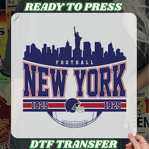 May include: A white DTF transfer featuring a navy blue skyline with the Statue of Liberty, the text "FOOTBALL NEW YORK 1925", and a football helmet. The words "READY TO PRESS" and "DTF TRANSFER" are also present.