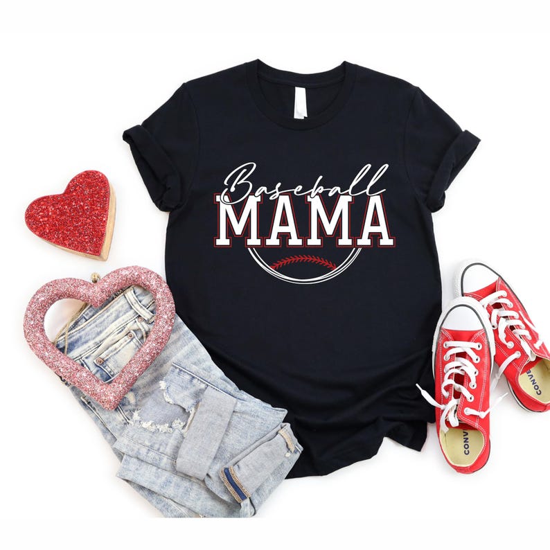 May include: Black t-shirt with the text "Baseball MAMA" in white and red lettering, with a baseball graphic. The image also includes a pair of blue jeans, red sneakers, and heart-shaped decorations.