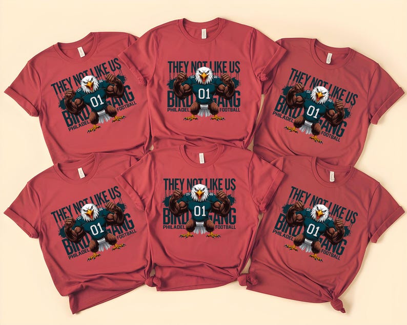 K&ouml;nnte beinhalten: Rote T-Shirts mit einer Grafik eines Adlers, der ein Football-Trikot mit der Nummer 01 tr&auml;gt. Auf den Shirts steht "THEY NOT LIKE US BIRD GANG PHILADELPHIA FOOTBALL."