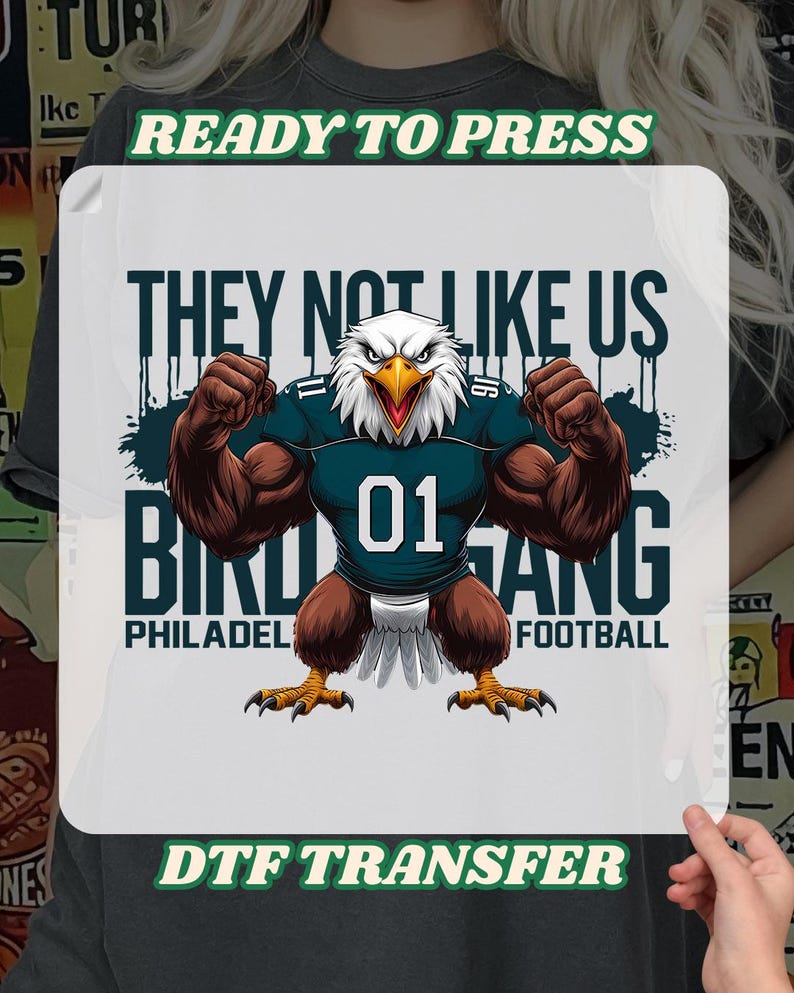 K&ouml;nnte beinhalten: DTF-Transfer mit einem muskul&ouml;sen Adler, der ein t&uuml;rkisfarbenes Football-Trikot mit der Nummer 01 tr&auml;gt. Der Text lautet "THEY NOT LIKE US" und "BIRD GANG PHILADELPHIA FOOTBALL". Die W&ouml;rter "READY TO PRESS" und "DTF TRANSFER" sind ebenfalls vorhanden.