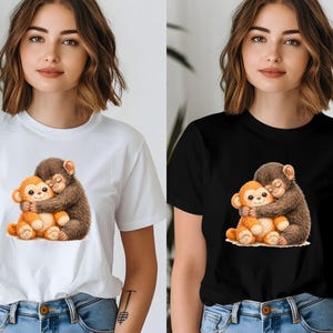 Op de afbeelding: Witte en zwarte T-shirts met een hartverwarmende illustratie van twee cartoonapen die elkaar omhelzen. Het ontwerp toont een bruine aap die een oranje aap omhelst, wat een gevoel van warmte en genegenheid cre&euml;ert. De shirts zijn gemaakt van zacht materiaal.