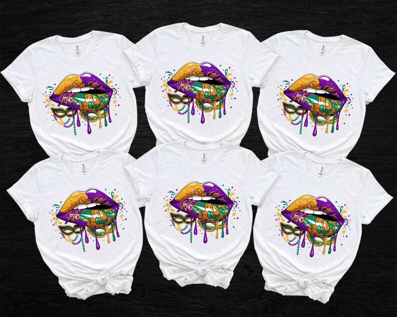 May include: Six white t-shirts with a colorful graphic of lips, a mask, and beads. The lips are gold and purple, with green and gold accents. The mask is green and gold, and the beads are purple and gold. The design has a dripping effect.