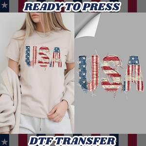 May include: A beige t-shirt with the word "USA" in a distressed American flag design. The image also shows a DTF transfer design with the text "READY TO PRESS" and "DTF TRANSFER".
