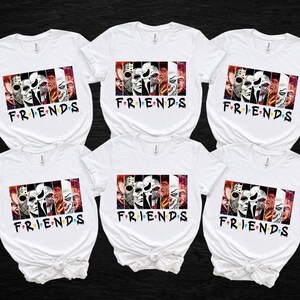 May include: White t-shirts with a graphic featuring horror movie characters and the word "FRIENDS" in a colorful font. The graphic is a collage of iconic horror movie villains. The shirts are arranged on a black background.