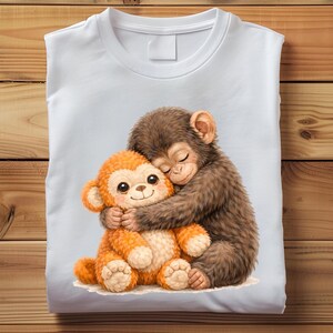 Op de afbeelding: Wit T-shirt met een aquarel illustratie van twee knuffelende apen. De ene aap is bruin en harig, de andere is oranje en pluche. Het ontwerp is gecentreerd op het shirt.