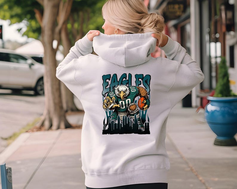 May include: A pale grey hoodie with a graphic of an eagle in a football uniform, with the text "EAGLES". The eagle is holding a football. The hoodie has a drawstring hood.