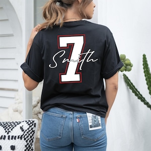 May include: Black t-shirt with the number 7 and the name "Smith" in white script. The number 7 has a red outline. The shirt is a casual style, suitable for everyday wear.