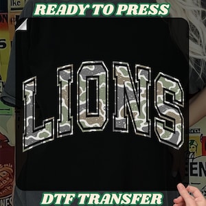 May include: Black t-shirt with the word "LIONS" in a camouflage design. The text "READY TO PRESS" is above the design, and "DTF TRANSFER" is below it. The shirt is displayed on a person.