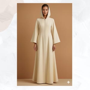 May include: A long, cream-colored hooded coat with a full-length zipper. The coat has wide sleeves and a flared skirt, creating a flowing silhouette. The model is wearing the coat, standing in front of a brown background.