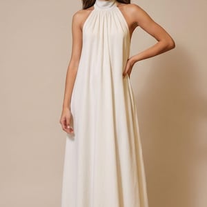 May include: A floor-length, ivory-colored dress with a halter neckline. The dress features a high, gathered neckline and a flowing, A-line skirt. The fabric appears to be a lightweight material, suitable for warmer weather. The dress is a solid color.