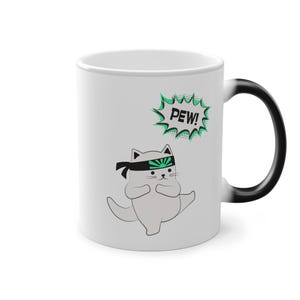 Könnte beinhalten: Weiße Keramik-Tasse mit einer Cartoon-Katze als Ninja mit einem schwarzen Stirnband und einem grün-schwarzen Design. Die Tasse hat das Wort "PEW!" in einer grünen Sprechblase.