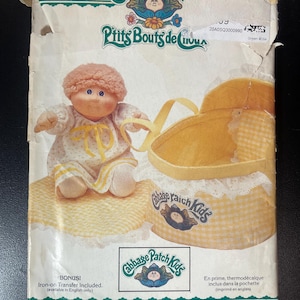 May include: Vintage Butterick Cabbage Patch Kids sewing pattern. The pattern features a doll with a yellow and white dress, a yellow bassinet, and the text "Cabbage Patch Kids" and "Ptits Bouts de Chou".